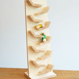 The Beck Cascading Tower Run Track with Race Cars placed on a wooden surface. The yellow and green cars are seen in motion on the track.