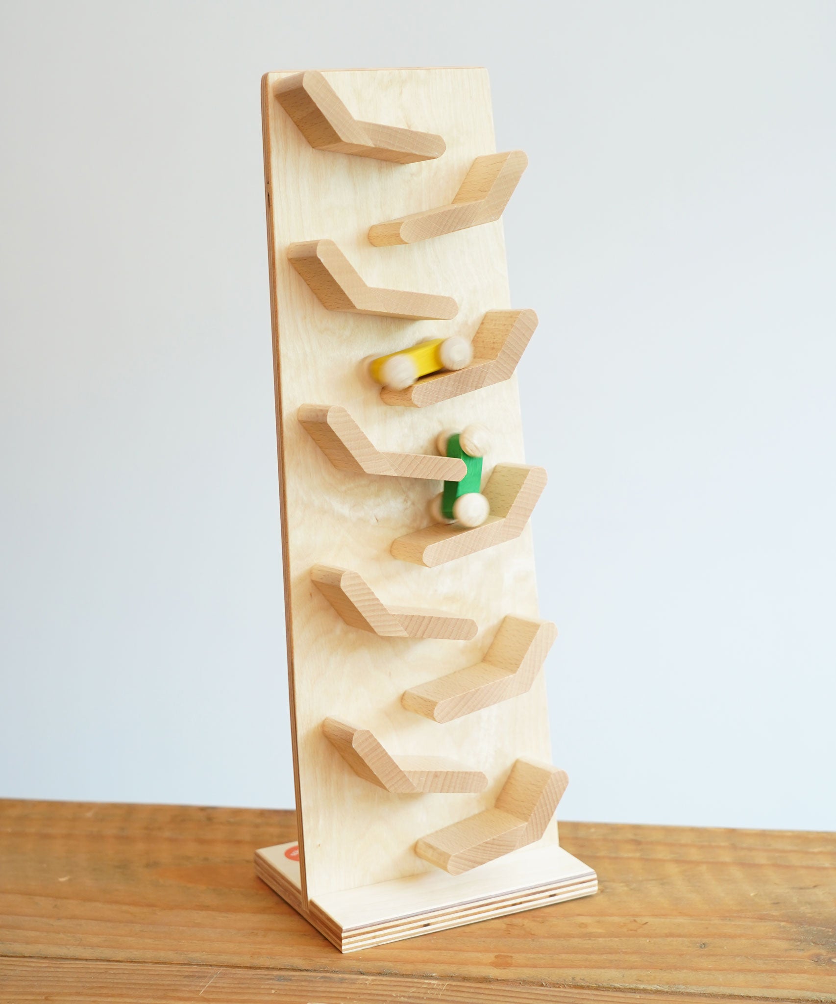 The Beck Cascading Tower Run Track with Race Cars placed on a wooden surface. The yellow and green cars are seen in motion on the track.