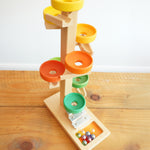 The Beck Toys Beech Wood Marble Run Plate Tower with Glockenspiel placed on a wooden surface. The set comes with 8 coloured glass marbles. 