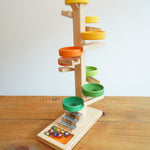 The Beck Toys Beech Wood Marble Run Plate Tower with Glockenspiel placed on a wooden surface. The set comes with 8 coloured glass marbles. 