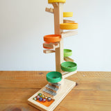 The Beck Toys Beech Wood Marble Run Plate Tower with Glockenspiel placed on a wooden surface. The set comes with 8 coloured glass marbles. 