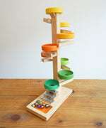 The Beck Toys Beech Wood Marble Run Plate Tower with Glockenspiel placed on a wooden surface. The set comes with 8 coloured glass marbles. 