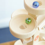 A close up of glass marbles, blurred in motion whilst they cascade down the Beck Toys Maple Wood Marble Run Plate Tower.