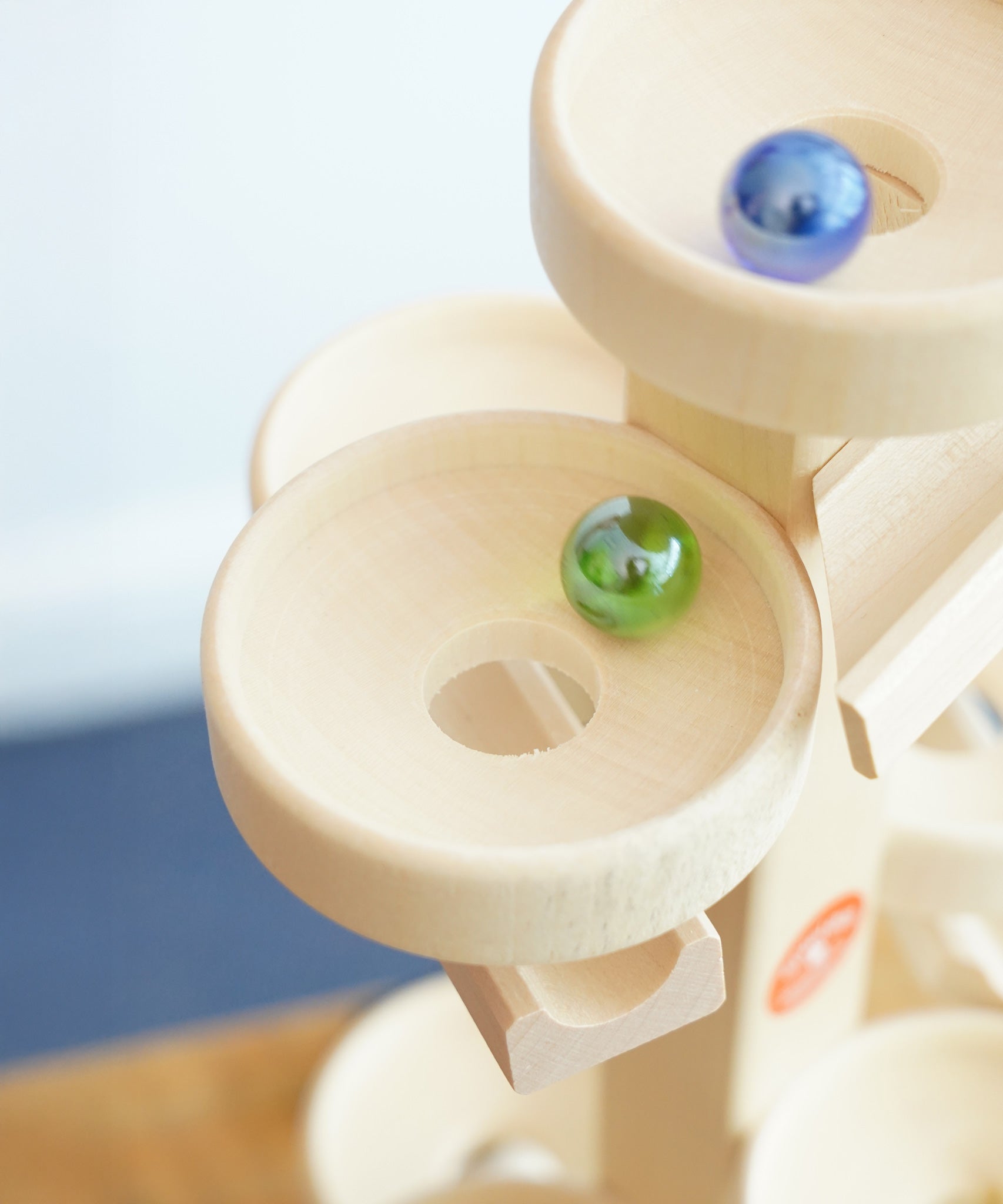 A close up of glass marbles, blurred in motion whilst they cascade down the Beck Toys Maple Wood Marble Run Plate Tower.