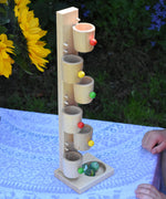 The Beck Toys Beech Wood Roller Cup Marble Run placed on a small table outdoors. A bunch of sunflowers can be seen to the side.