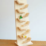 The Beck wooden Toy Cascading Tower Run Track with Race Cars placed on a wooden surface. The yellow and green cars are seen in motion on the track.