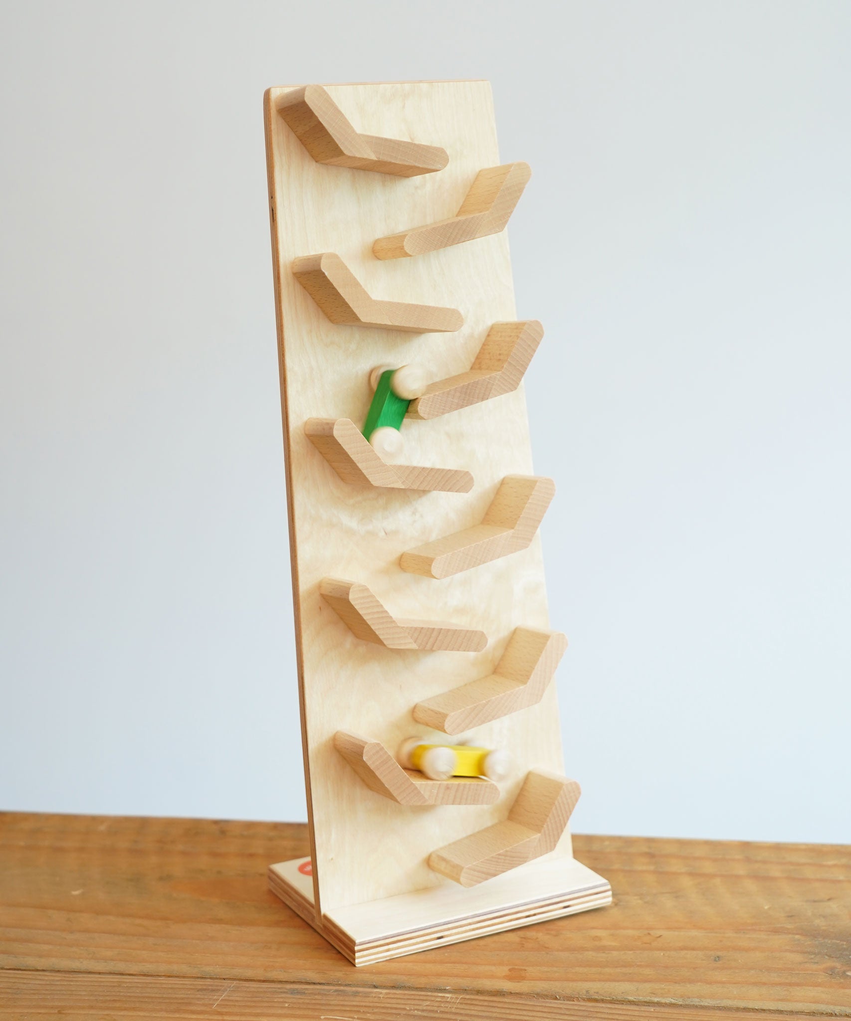The Beck wooden Toy Cascading Tower Run Track with Race Cars placed on a wooden surface. The yellow and green cars are seen in motion on the track.