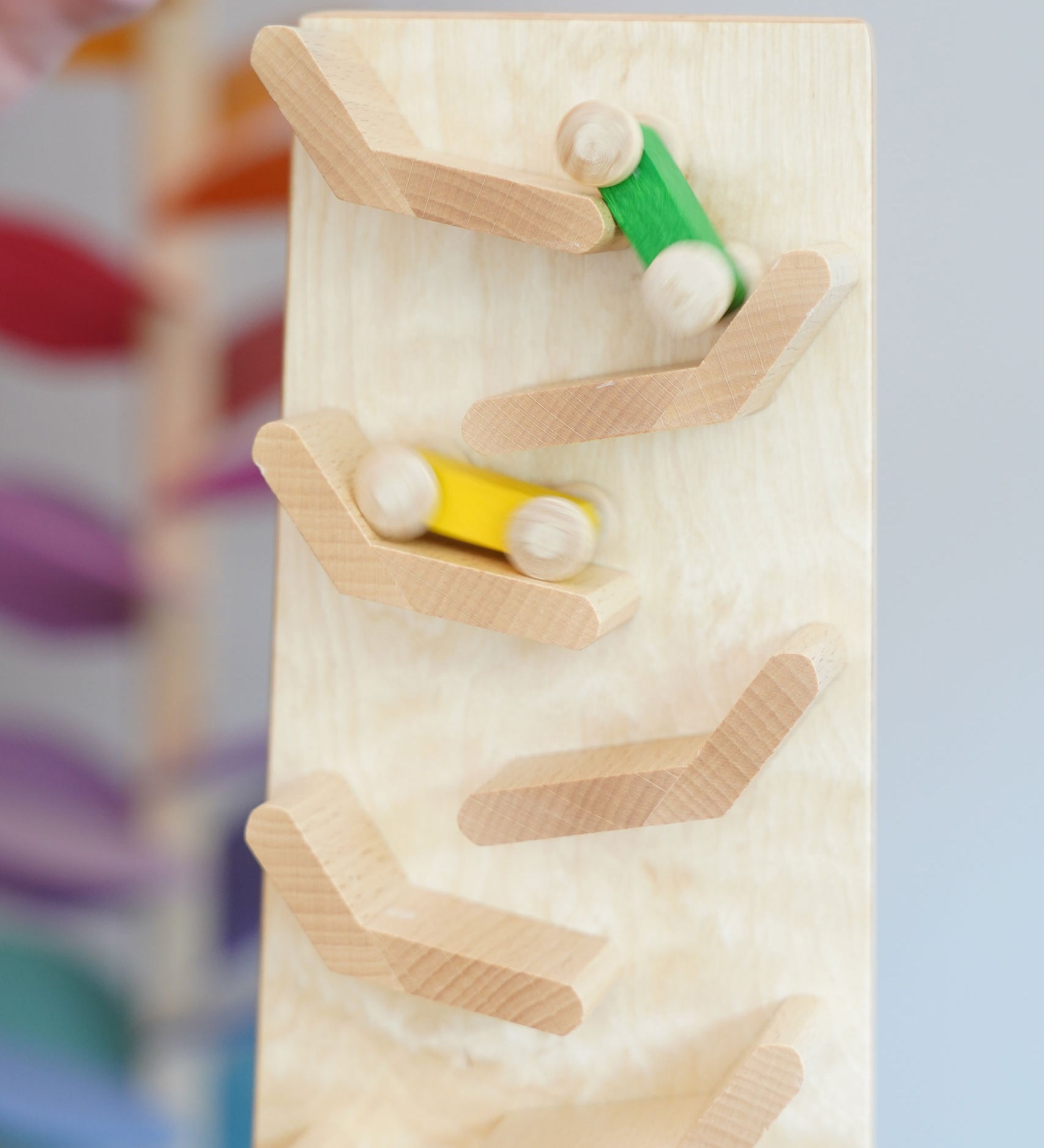 A close up of the yellow and green coloured wooden racing cars racing down the Beck Toys Cascading Tower Race Track. The cars are slightly blurred in motion. 