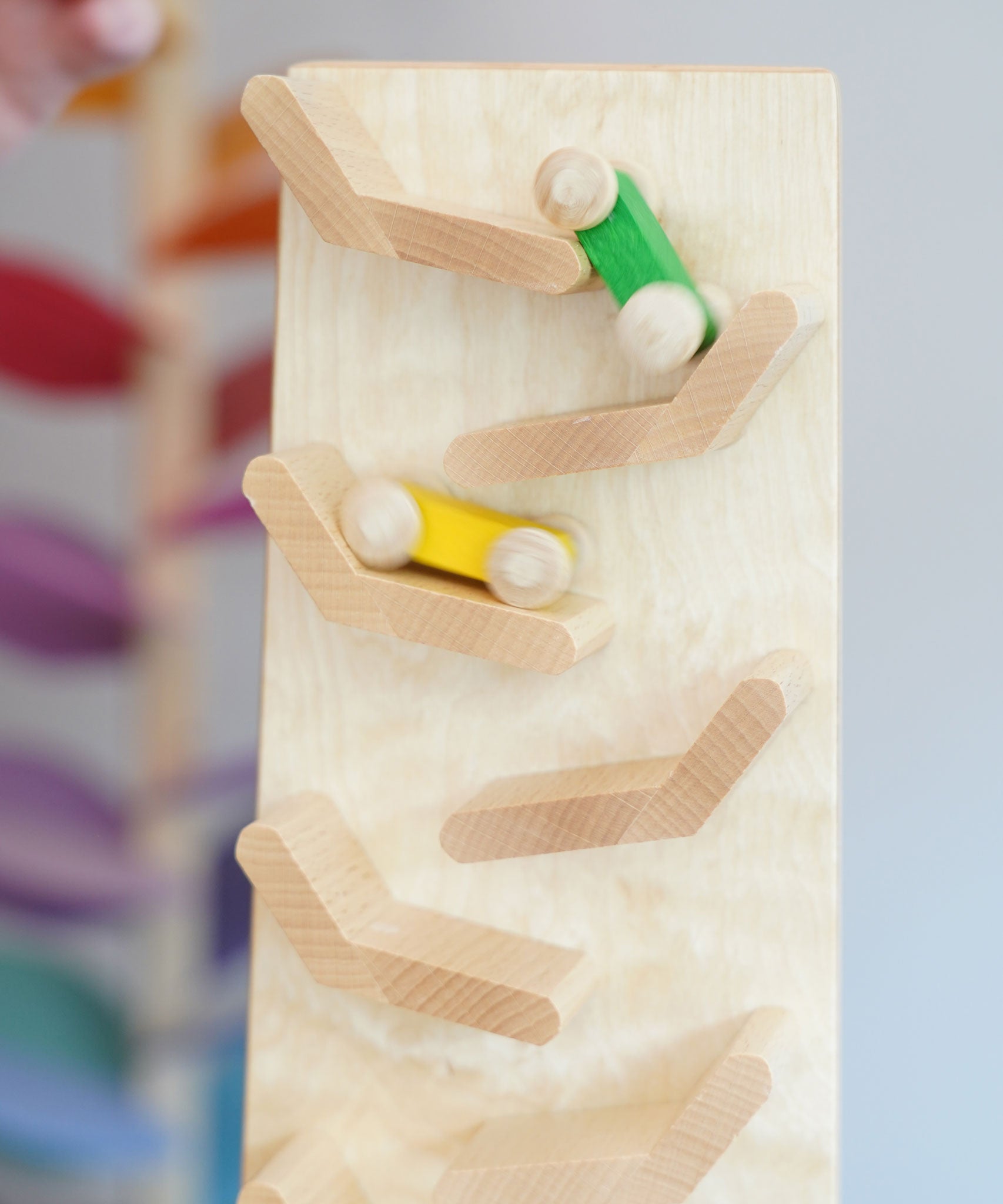 A close up of the yellow and green coloured wooden racing cars racing down the Beck Toys Cascading Tower Race Track. The cars are slightly blurred in motion. 