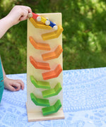 A close up of a child's hand placing the car train on the track. The Beck Toys Beechwood Cascading ‘Tower Running Track’ with Millipede Car Train toy has coloured ramps.