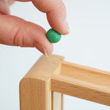 A close up of a green coloured, small clay marble in an adult's hand. The clay marbles are included in the Beck Toys Chimes Marble Run Track Set.