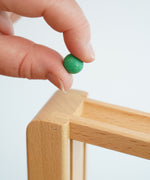 A close up of a green coloured, small clay marble in an adult's hand. The clay marbles are included in the Beck Toys Chimes Marble Run Track Set.
