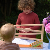 A child playing with the Beck Toys Chimes Marble Run Track. A younger child is standing in front observing one of the clay marbles going down the track.