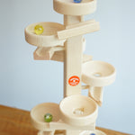 Glass marbles cascading down the Beck Toys Maple Wood Marble Run Plate Tower.