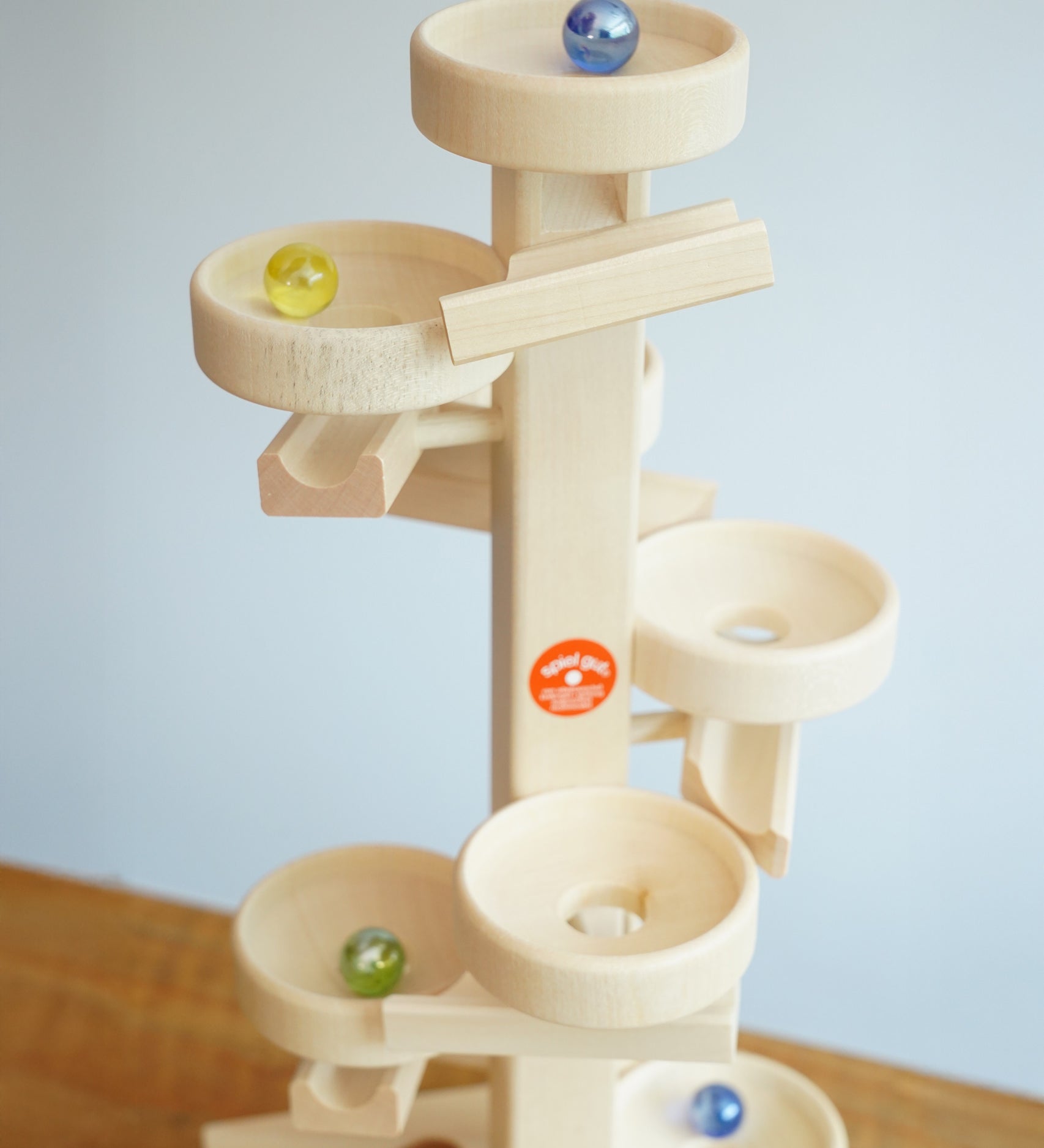 Glass marbles cascading down the Beck Toys Maple Wood Marble Run Plate Tower.