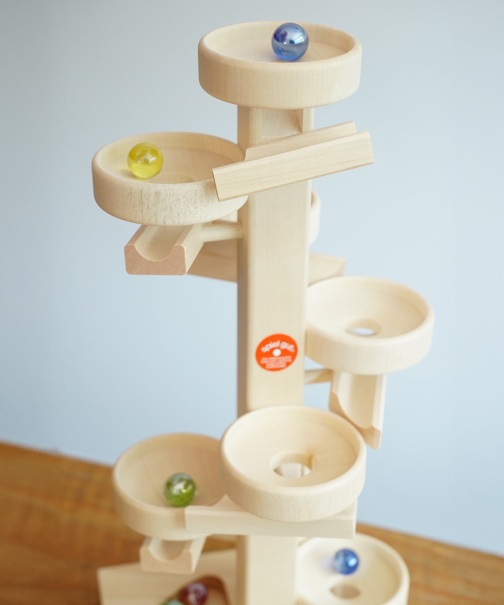 Glass marbles cascading down the Beck Toys Maple Wood Marble Run Plate Tower.