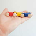 A close up of the colourful wooden millipede car train from Beck Toys in an adult's hand.