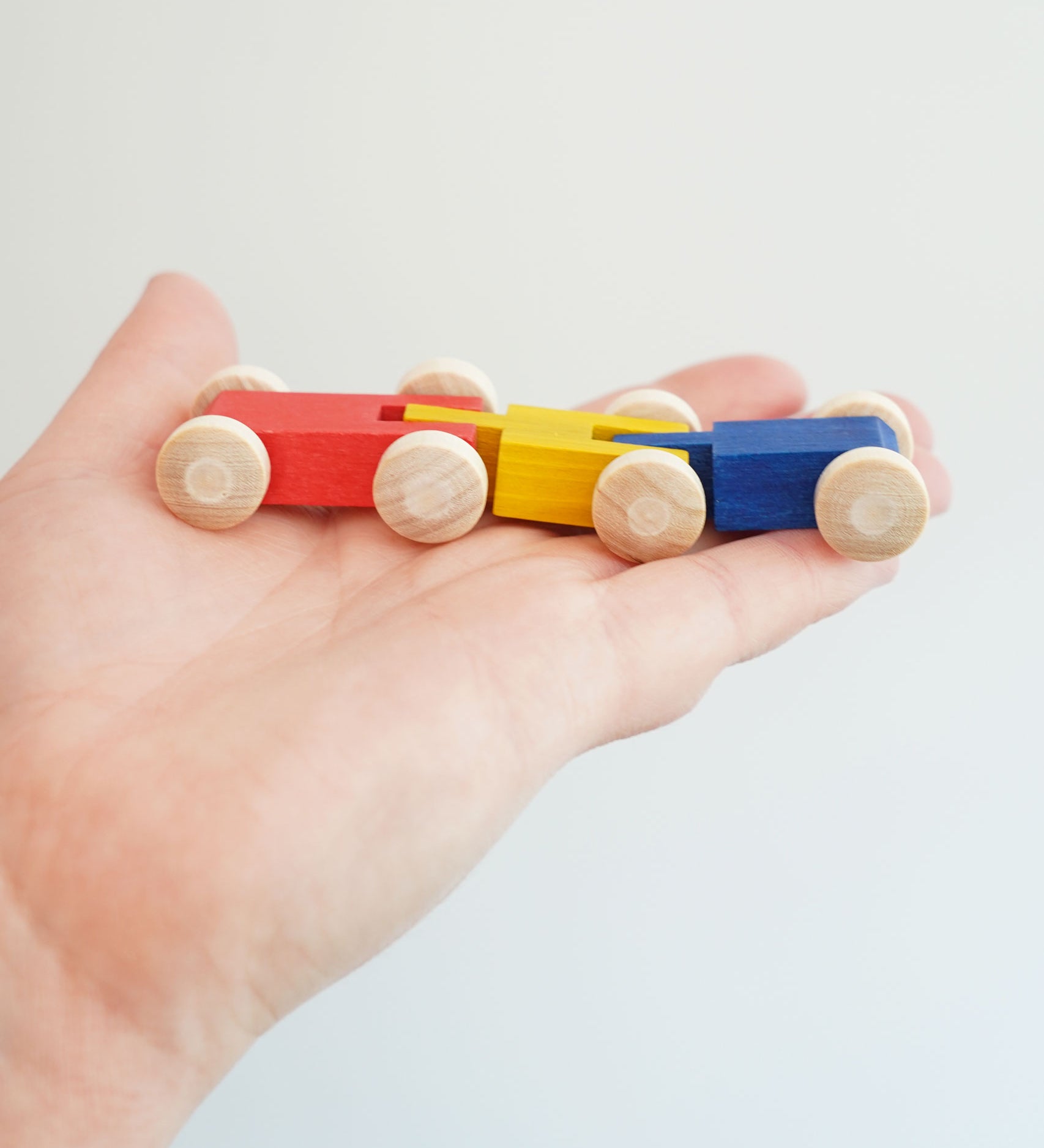 A close up of the colourful wooden millipede car train from Beck Toys in an adult's hand.