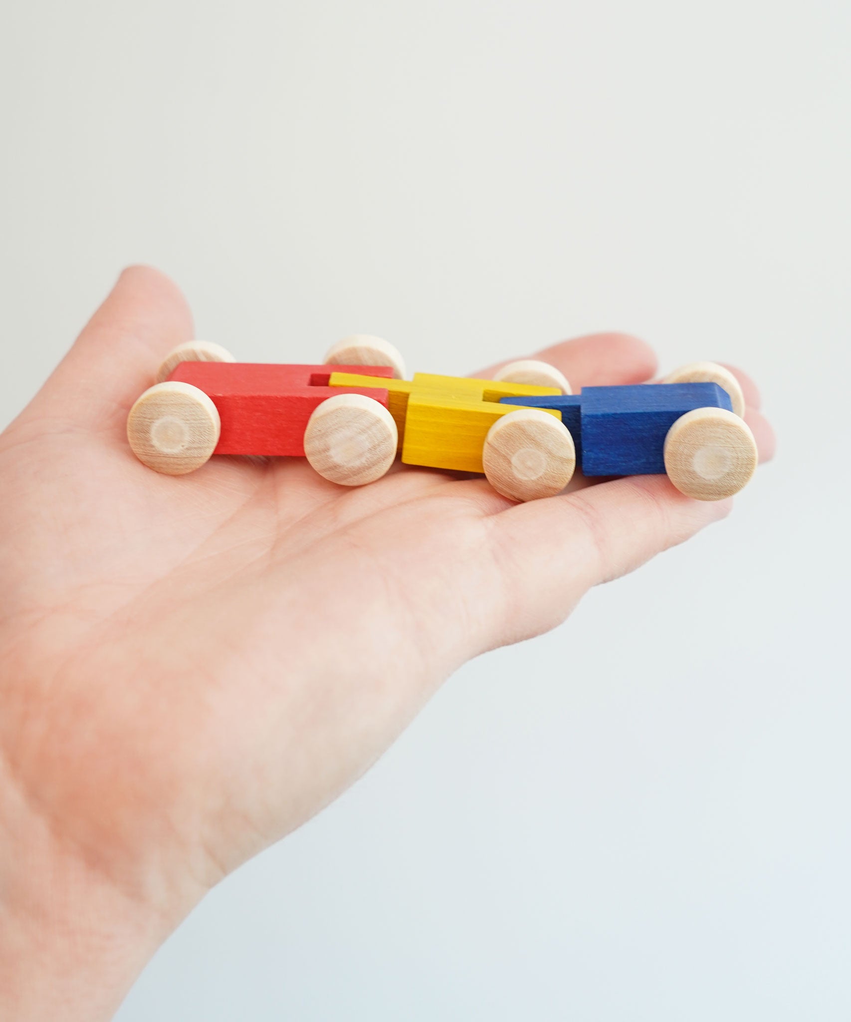A close up of the colourful wooden millipede car train from Beck Toys in an adult's hand.
