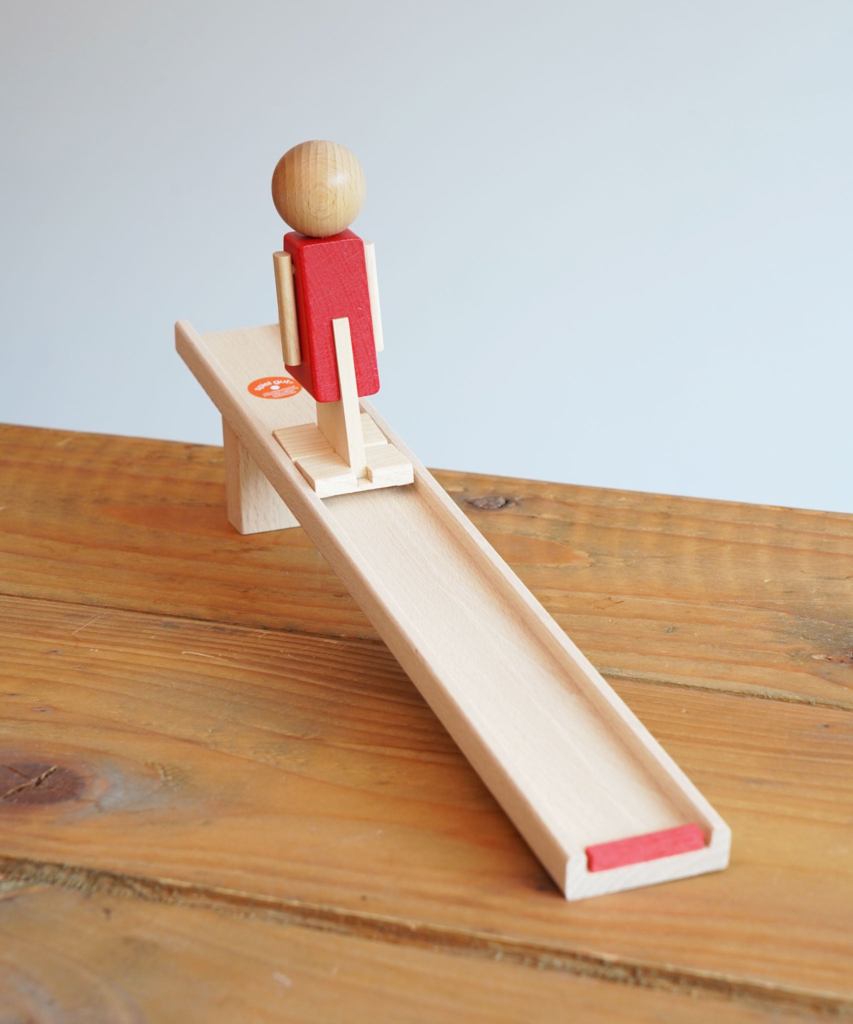 Beck Toys Nurmi Ramp Walker Wooden Toy placed on a wooden surface. The red colured wooden figure has been placed onto the ramp.