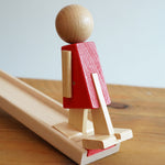 A close up of the wooden walking figure standing on the end of the wooden ramp from the Beck Toys Nurmi Ramp Walker Wooden Toy Set. 