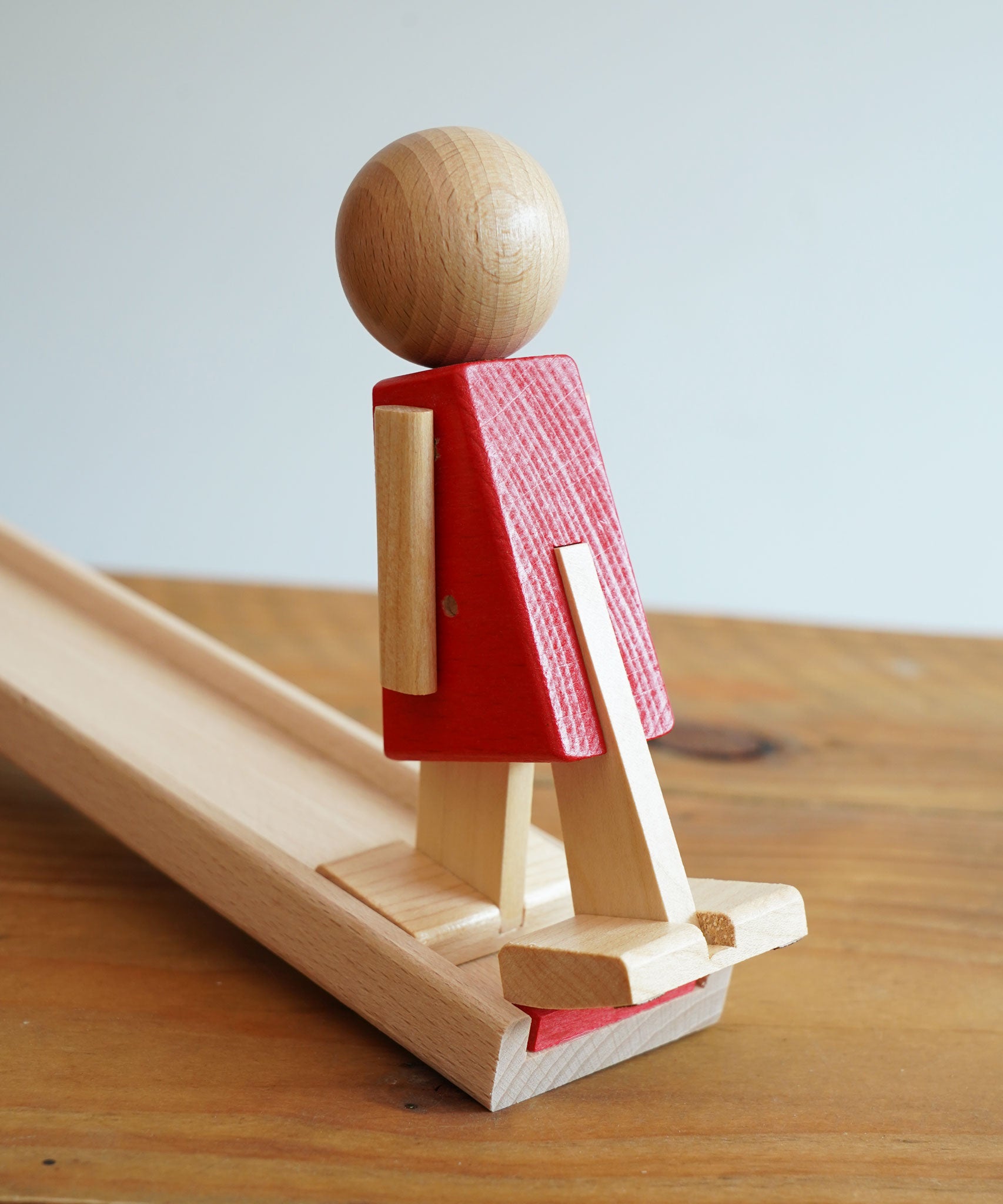 A close up of the wooden walking figure standing on the end of the wooden ramp from the Beck Toys Nurmi Ramp Walker Wooden Toy Set. 