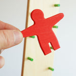 A close of the red coloured wooden person figure from the  Beck wooden Toys Wobbler in an adult's hand. 