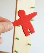 A close of the red coloured wooden person figure from the  Beck wooden Toys Wobbler in an adult's hand. 