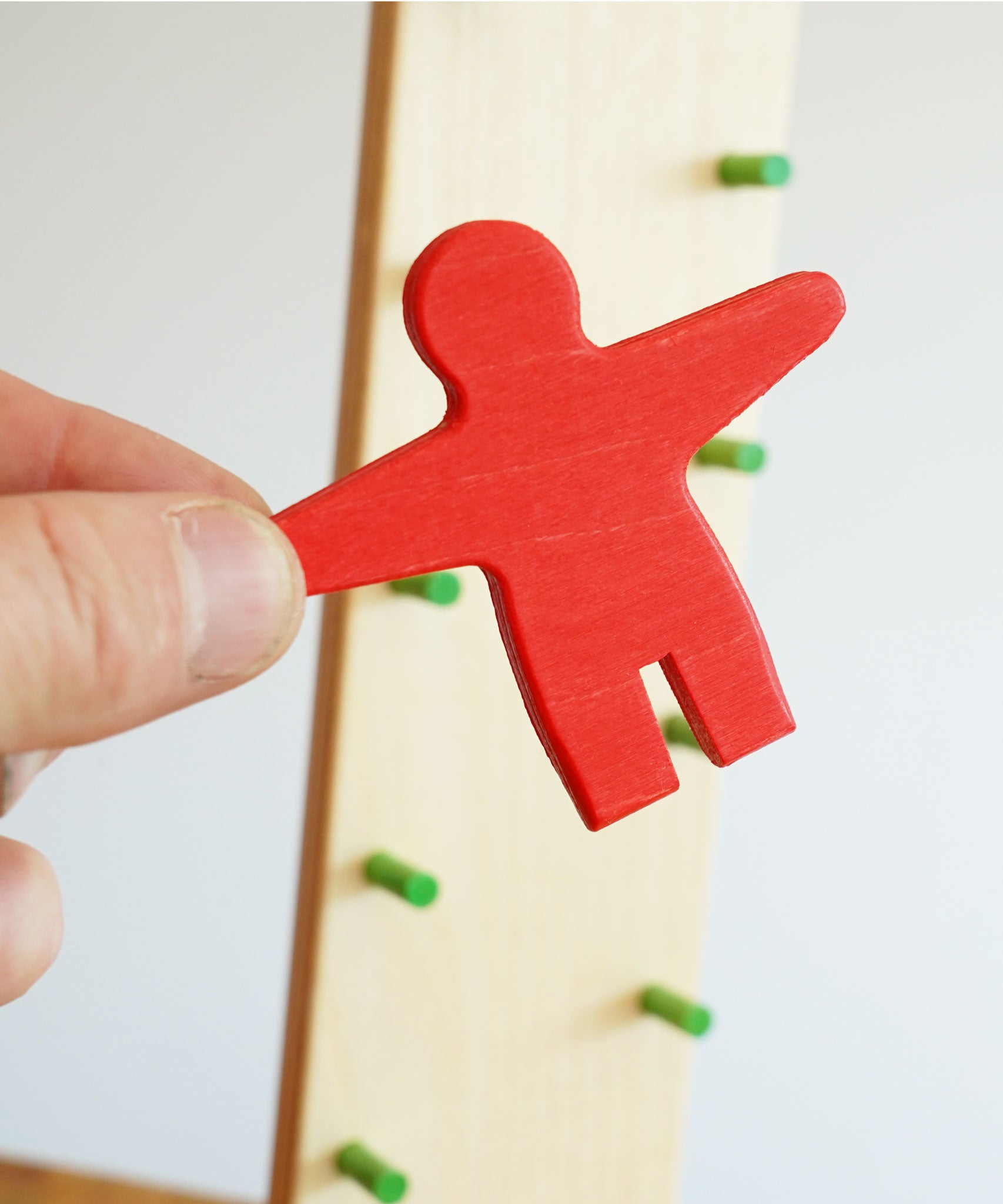A close of the red coloured wooden person figure from the  Beck wooden Toys Wobbler in an adult's hand. 