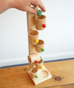 An adult's hand placing a glass marble into the first cup on the Beck Toys Beech Wood Roller Cup Marble Run.