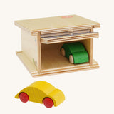Beck Holzspielzeug Wooden Small Toy Car Garage shown with door open and one car inside and one outside. This wooden toy car garage is part of a wide range of toy vehicles and accessories available at Babipur.