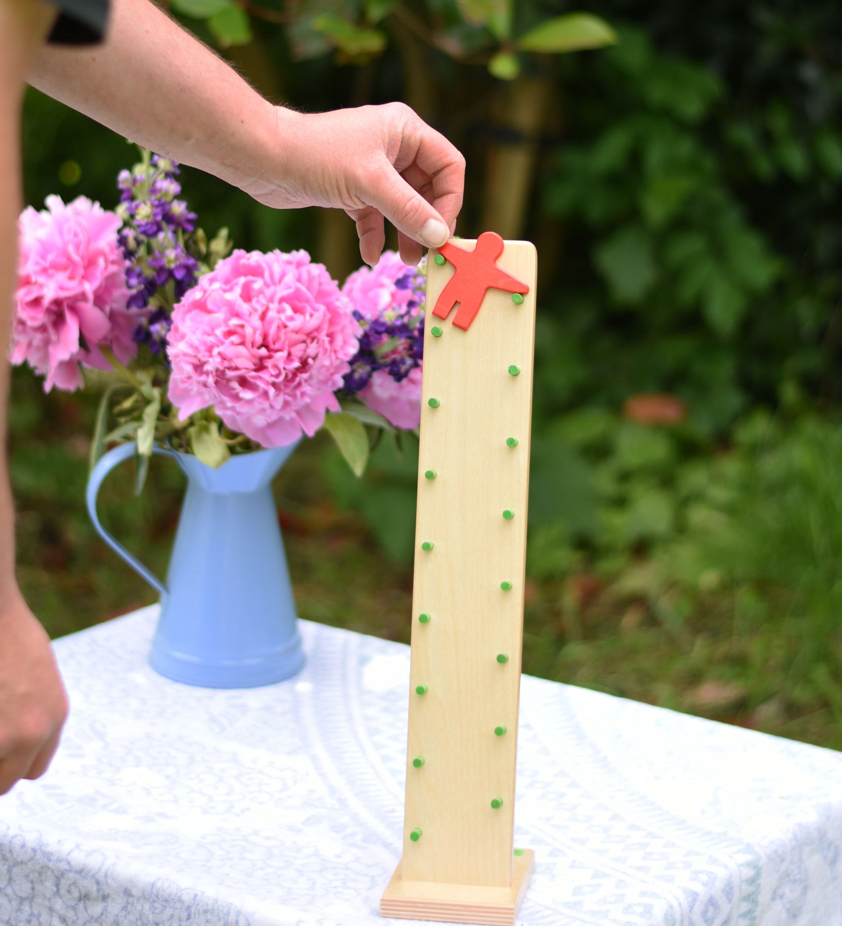 An adult placing the red coloured wooden figure on the Beck Toy Wobbler wooden tumbling toy frame. 