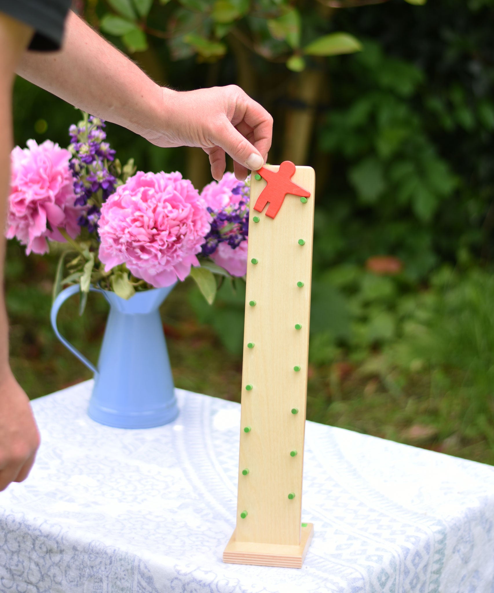 An adult placing the red coloured wooden figure on the Beck Toy Wobbler wooden tumbling toy frame. 