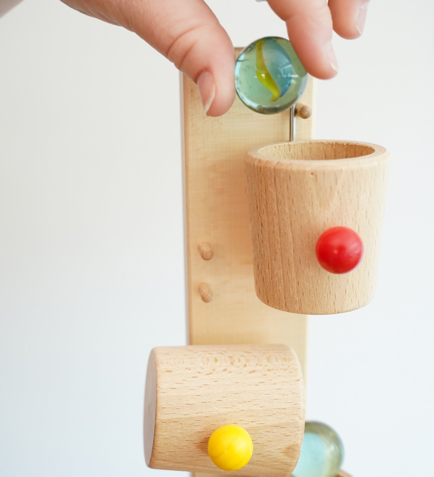A close up of an adult's hand placing a glass marble into the first cup on the Beck Toys Beech Wood Roller Cup Marble Run. 