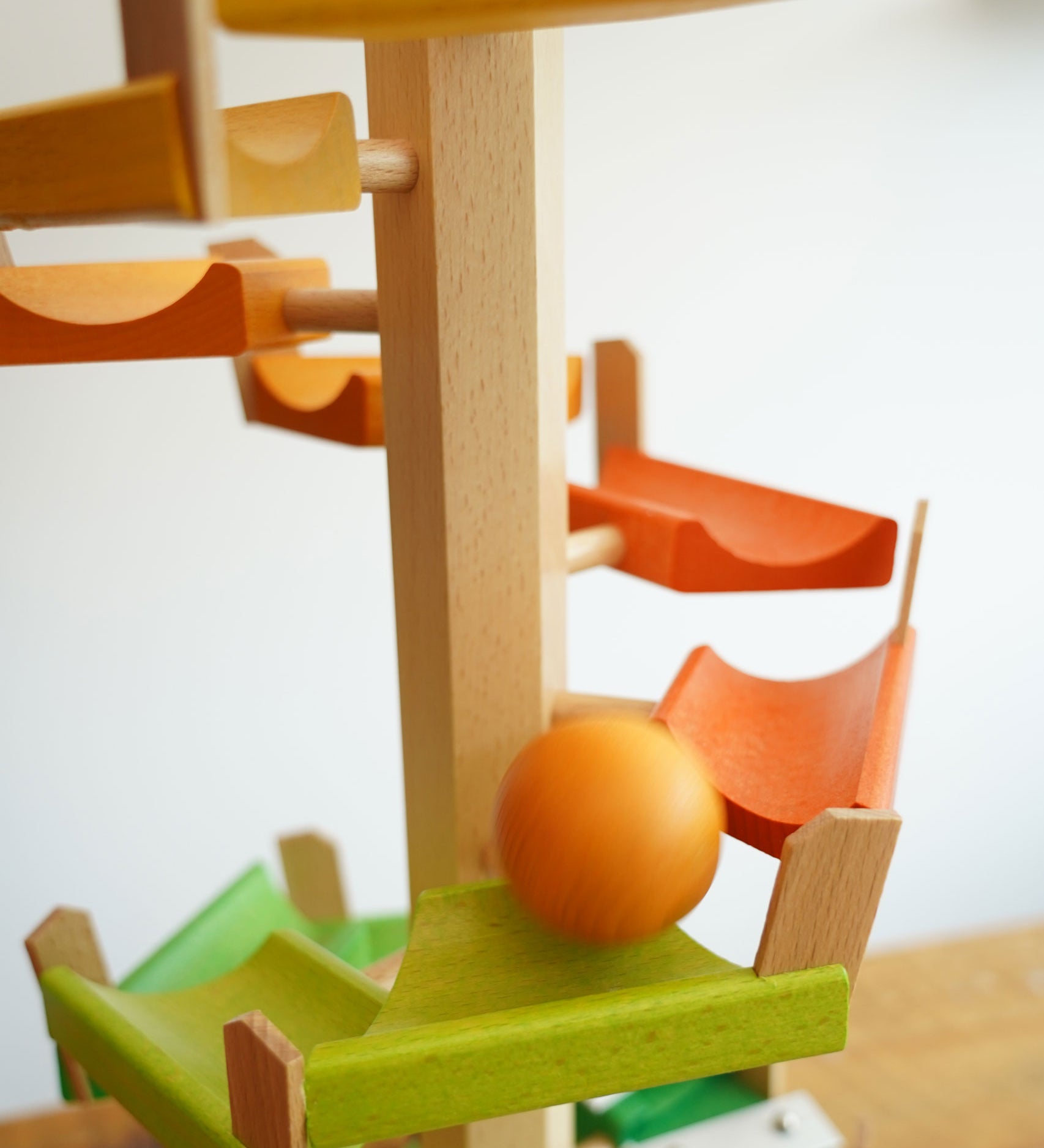 A orange coloured ball cascading down the track of the Beck Wooden musical chimes Ball Run. The ball is blurred in motion as it races down the wooden ramp pieces.