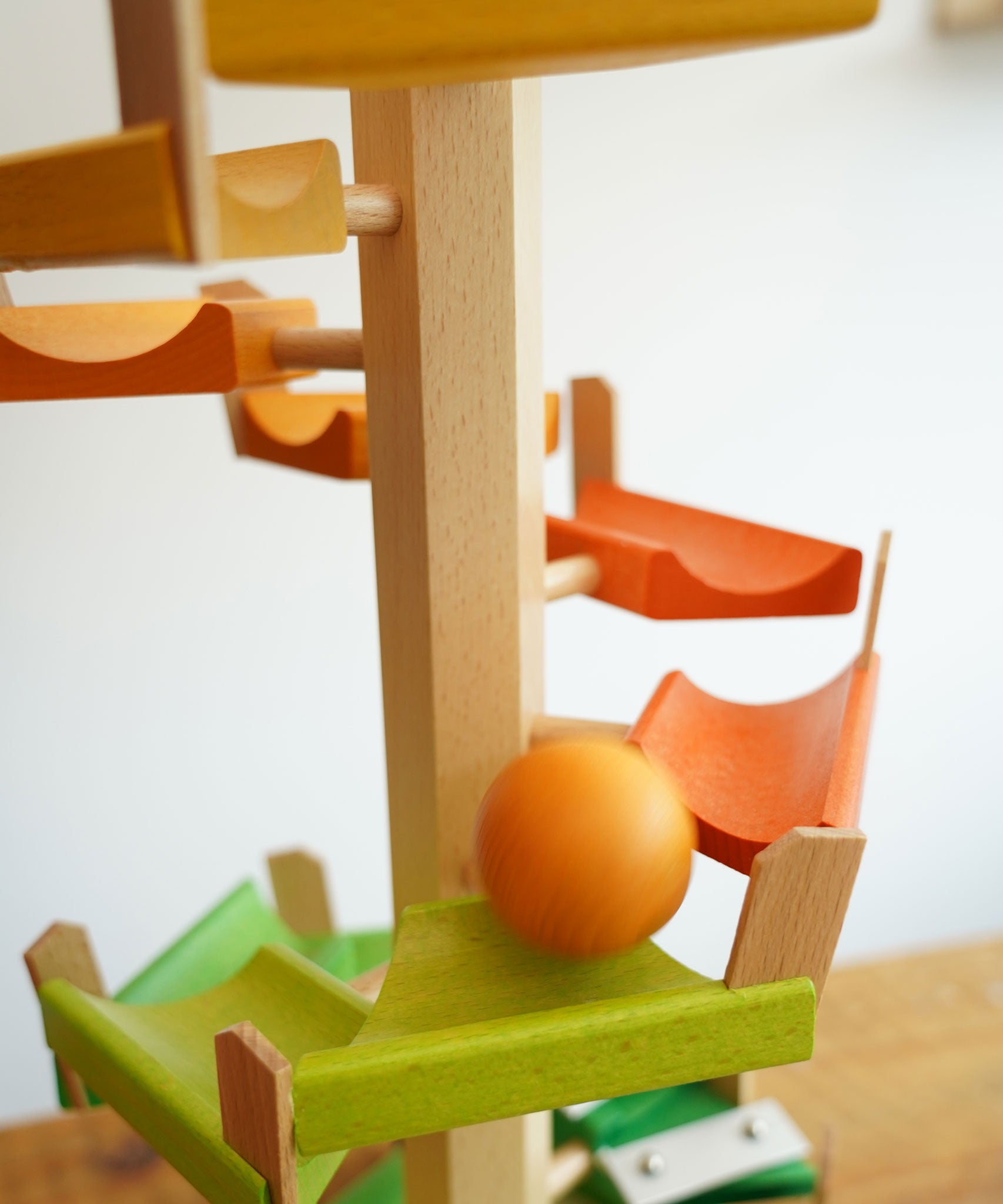 A orange coloured ball cascading down the track of the Beck Wooden musical chimes Ball Run. The ball is blurred in motion as it races down the wooden ramp pieces.