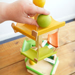 An adult's hand placing a green coloured ball on the track of the Beck Wooden musical chimes step tower ball run toy from Beck Toys. 