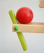 A close up of the red ball on the Beck Ball Run Musical Track. The wooden ball is blurred in motion as it aces down the wooden ramps on the ball run.