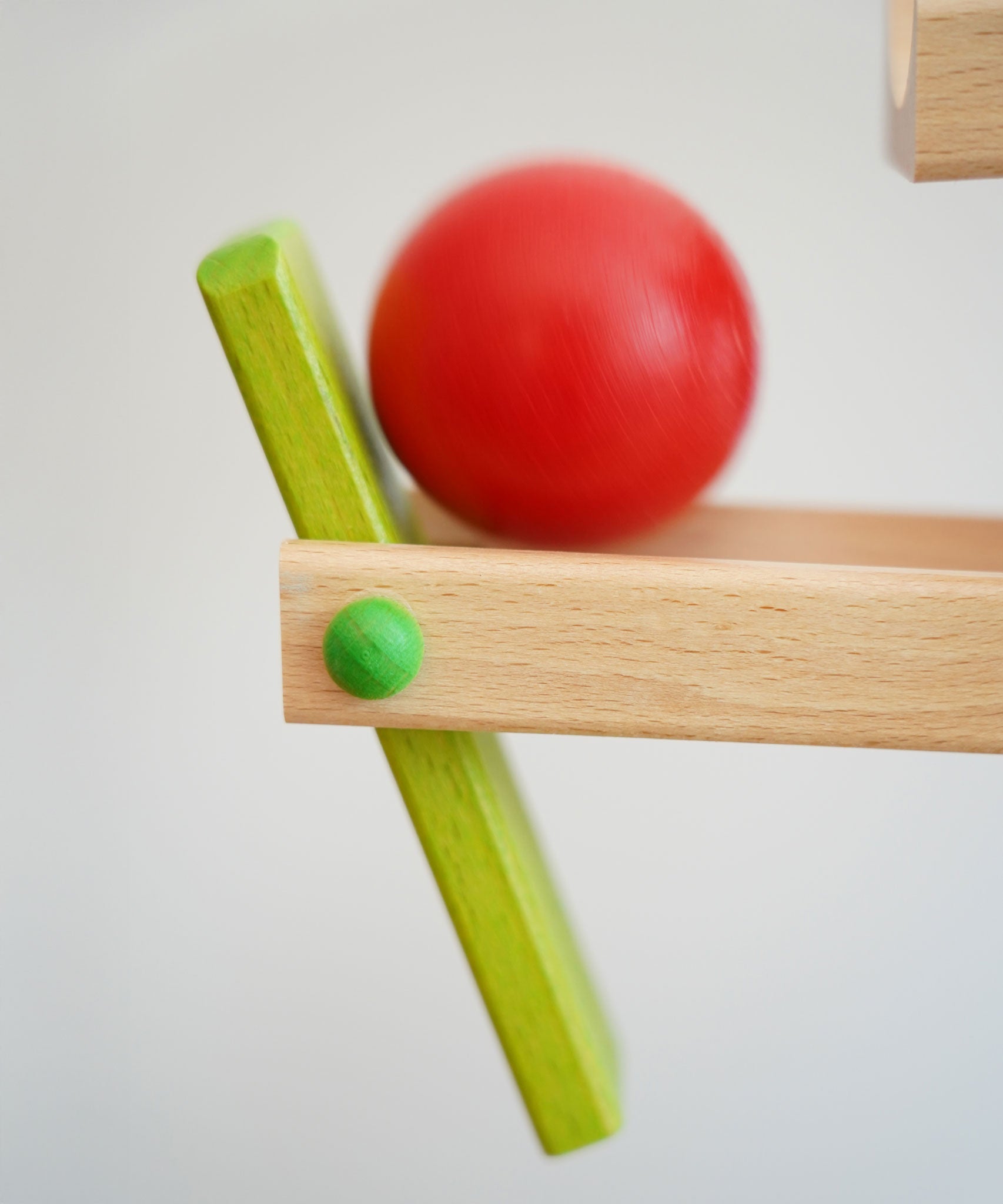A close up of the red ball on the Beck Ball Run Musical Track. The wooden ball is blurred in motion as it aces down the wooden ramps on the ball run.
