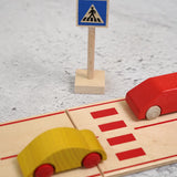 A Beck wooden pedestrian crossing  sign standing near a road set with vehicles on top 