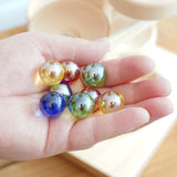 A close up of 8 coloured glass marbles from the Beck Toys Maple Wood Marble Run Plate Tower set in an adult's hand. 