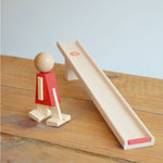 The Beck Toys Nurmi Ramp Walker Wooden Toy placed on a wooden surface, the walking figure has been placed next to the wooden ramp.