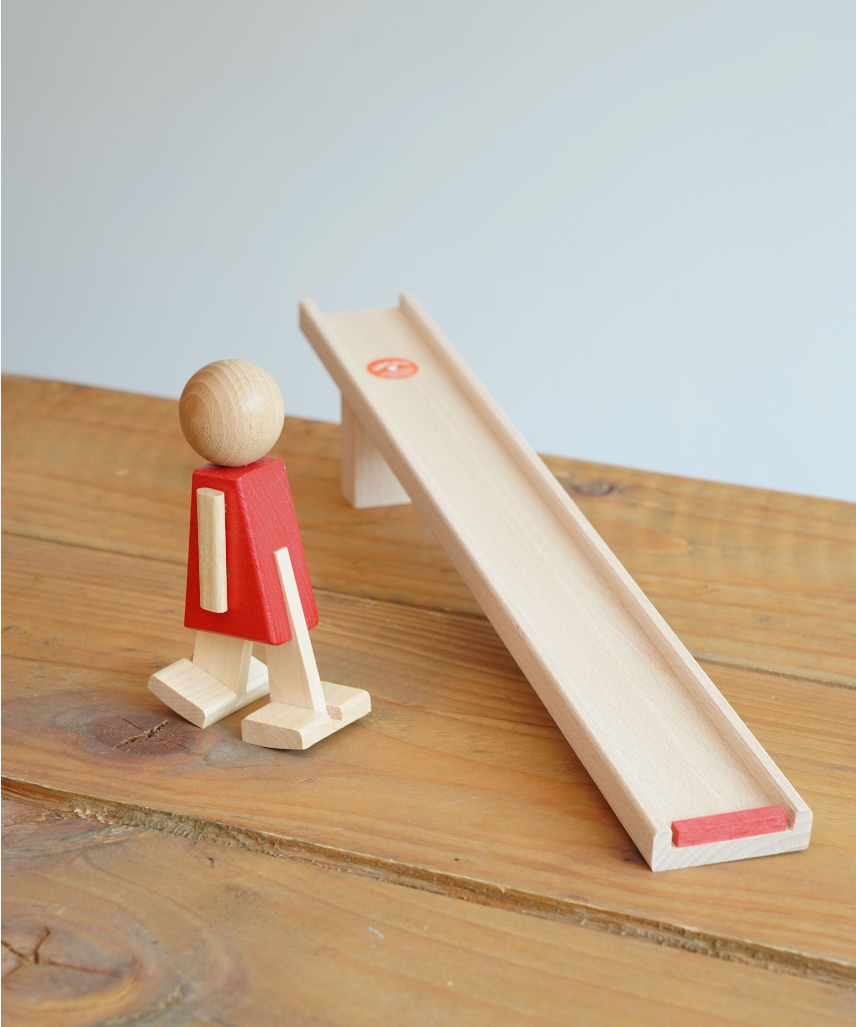 The Beck Toys Nurmi Ramp Walker Wooden Toy placed on a wooden surface, the walking figure has been placed next to the wooden ramp.
