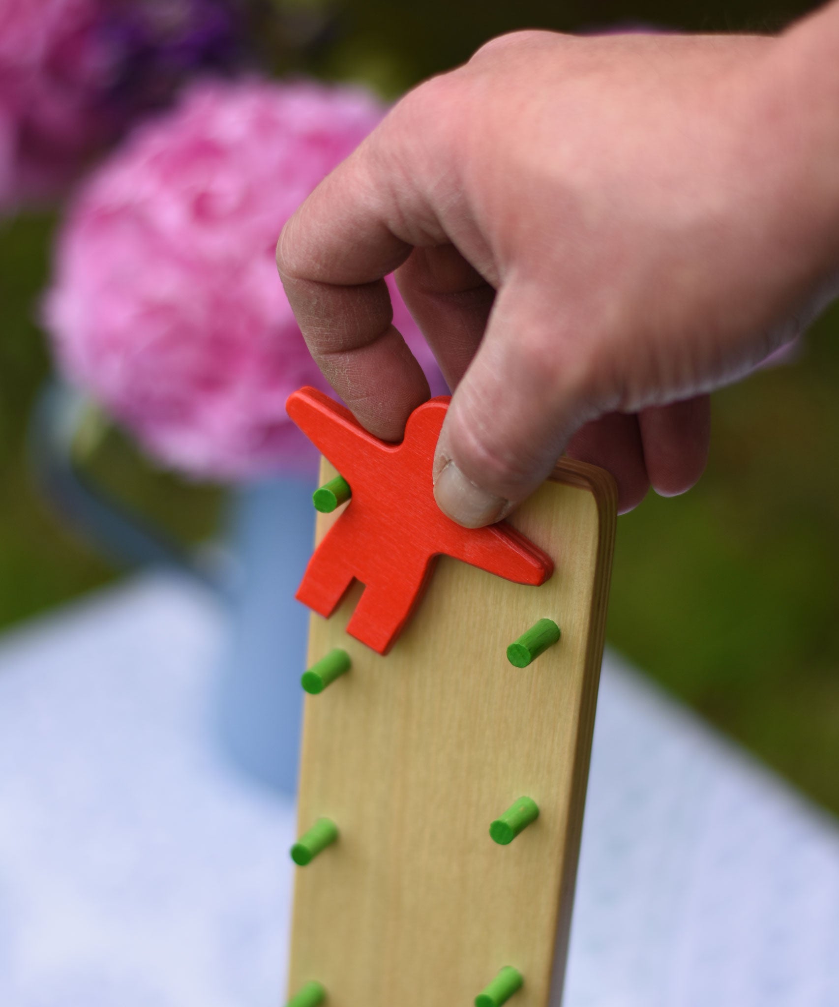 A close up of an adult's hand placing the red coloured wooden figure on the Beck Toy Wobbler wooden tumbling toy frame. 