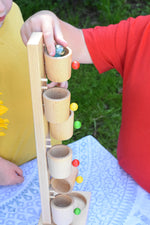 A close up of a child's hand placing a glass marble into the top cup of the Beck Toys Beech Wood Roller Cup Marble Run.