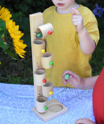 Children playing with the Beck Toys Beech Wood Roller Cup Marble Run. A glass marble can be seen blurred in motion as it transfers from one wooden cup to the next.