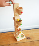 An adult's hand placing a glass marble into the first cup on the Beck Toys Beech Wood Roller Cup Marble Run.