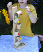 A child playing with the Beck Toys Beech Wood Roller Cup Marble Run. Marbles can be seen cascading down into the wooden cups.