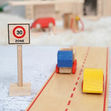 A Beck wooden 30 speed limit traffic sign standing near road pieces with vehicles on top and a toy petrol station in the background.