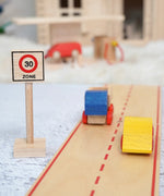 A Beck wooden 30 speed limit traffic sign standing near road pieces with vehicles on top and a toy petrol station in the background.